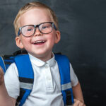 Young boy with a backpack on standing in front of chalk board