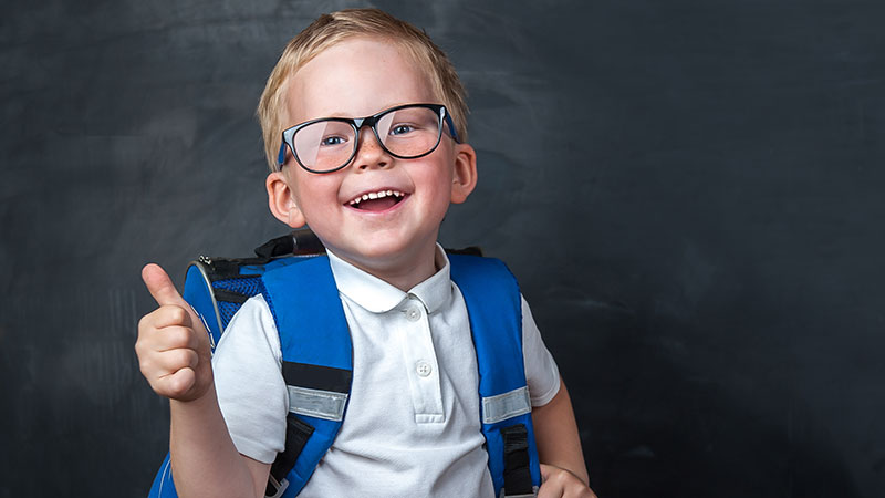 Young boy with a backpack on standing in front of chalk board