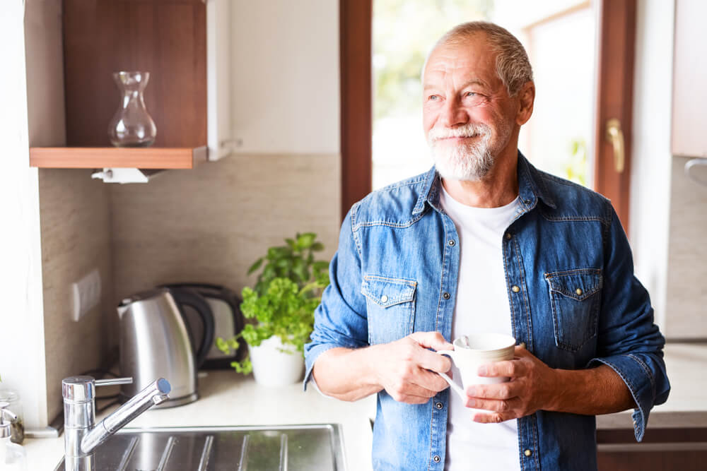 Happy senior man holding a cup of coffee in the kitchen.